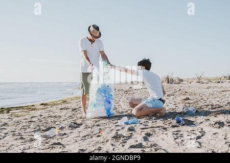 Groupe d'amis activistes collectant des déchets plastiques sur la plage. Les gens nettoyant la plage, avec des sacs. Concept de conservation de l'environnement et de l'océan Banque D'Images