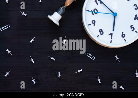 Horloge blanche, sablier et épingles sur fond en bois noir. Vue de dessus. CopySpace. Concept d'éducation ou d'entreprise. Banque D'Images