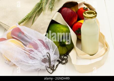 Sacs à provisions en coton avec légumes et fruits et une bouteille de lait en verre sur fond de bois blanc. Concept écologique et sans gaspillage. Banque D'Images