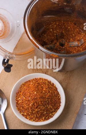 piment rouge séché moulu, poudre de poivre épicée sur une assiette, vue rapprochée prise par le dessus, tasse à moulin à café en arrière-plan Banque D'Images
