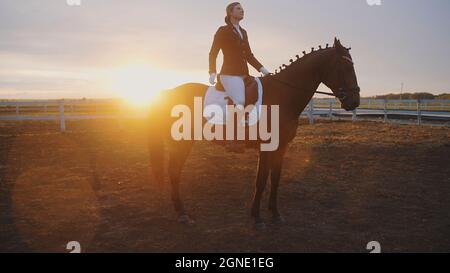 une jeune belle femme est assise sur un cheval, et derrière elle se trouve le coucher du soleil. Photo de haute qualité Banque D'Images