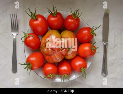 Présentation de steak fraîchement récolté et de tomates roma sur l'assiette avec couteau et fourchette Banque D'Images