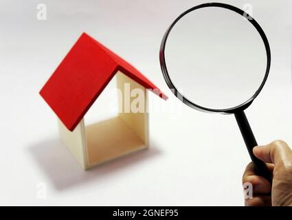 Une main d'homme tient une loupe sur une maison miniature. Concept de recherche immobilière. Idée d'inspection de maison. Banque D'Images