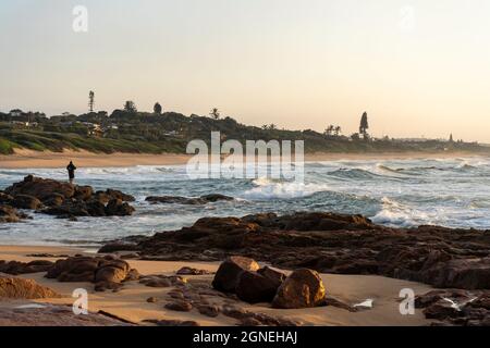Pêcheur solitaire sur les rochers pendant un beau lever de soleil sur la plage. Durban, côte est, Afrique du Sud. Photo de haute qualité Banque D'Images