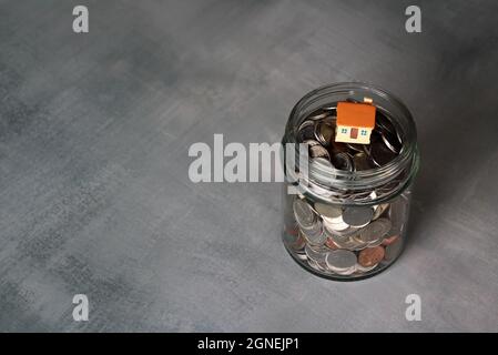Concept immobilier, immobilier et financier. Gros plan de pièces de monnaie dans un pot en verre avec maison miniature. Copier l'espace pour le texte Banque D'Images