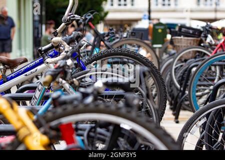 Vélos dans le centre ville de Cambridge porte-vélos - des roues toutes dans une rangée - des bâtiments flous et quelques personnes dans le fond Banque D'Images