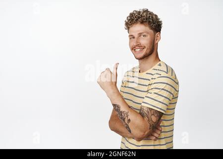 Un jeune homme attrayant avec une barbe et une coiffure blonde, montre les pouces avec un visage fier satisfait, souriant heureux, louant et complimentant, par exemple Banque D'Images