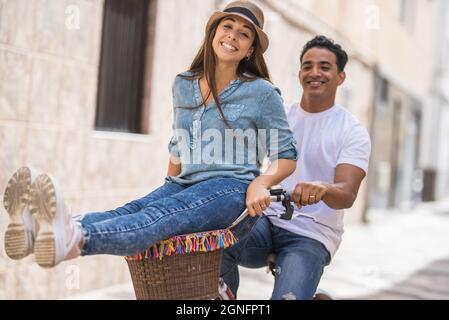 Joyeux couple à vélo en plein air dans la ville. Homme avec une femme ravie assis sur un guidon tout en faisant du vélo en ville. Couple insouciant en train de profiter de la bibi Banque D'Images