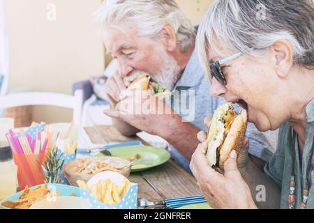 Couple senior prenant un morceau de hamburger au restaurant. Couple déjeuner au café. Un vieux couple avec un sandwich à cheveux gris au restaurant en plein air duri Banque D'Images