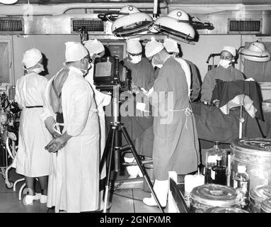 Angleterre. 1959. Un groupe de chirurgiens agissant sur un patient tout en étant photographié à l'aide d'une caméra plaque vintage. Banque D'Images