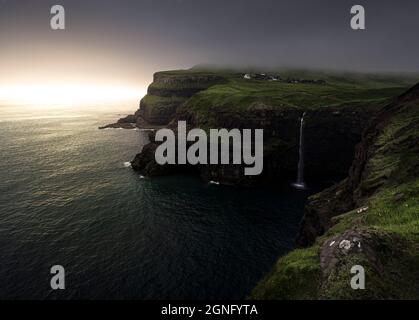 Gasadalur / Mulafossur Waterfall pendant un coucher de soleil brumeux/brumeux sur les îles Féroé lors d'une journée d'été verdoyante et luxuriante. Banque D'Images
