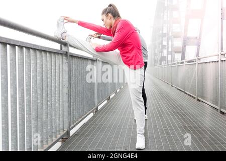 un jeune couple de coureurs étire leurs muscles après une course sur un pont métallique Banque D'Images