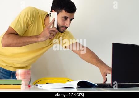 homme d'affaires debout près de la table avec l'ordinateur sur elle, il regarde et pointe vers l'écran. deux étudiants ont une conversation par téléphone et la préparation Banque D'Images