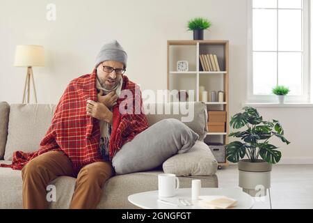 Homme d'âge moyen qui a le rhume ou la grippe commune assis sur le canapé à la maison et la toux Banque D'Images