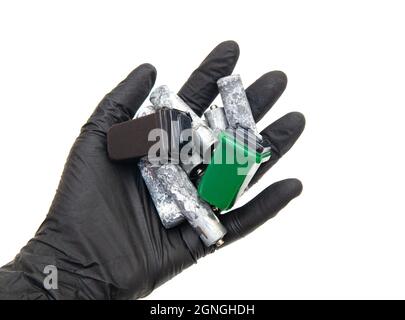 Gros plan d'une main humaine dans un gant en nitrile noir contenant des piles de type AA corrodées et des poubelles miniatures isolées sur fond blanc. Banque D'Images