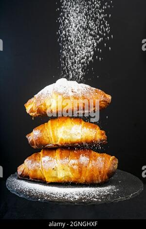 3 croissants en poudre saupoudrés de sucre isolés sur du noir Banque D'Images