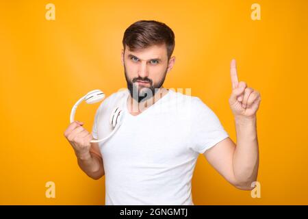 homme barbu tenant un casque de musique blanc à la main, montrant le pouce vers le haut. Banque D'Images