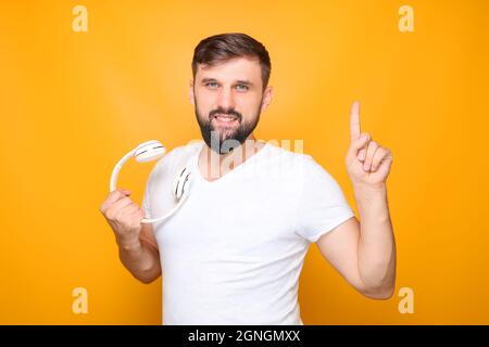 homme barbu tenant un casque de musique blanc à la main, montrant le pouce vers le haut. Banque D'Images