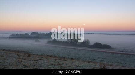 une brume matinale empli la vallée avec la lune de neige basse dans le ciel du lever du soleil Banque D'Images