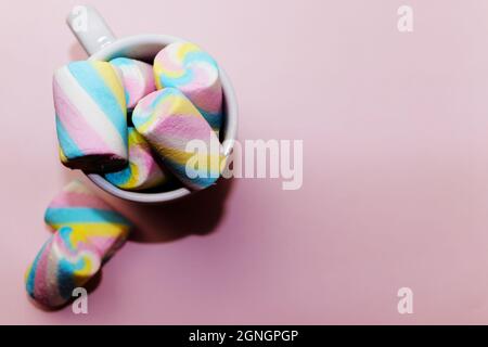 Des bonbons guimauves colorés dans une tasse blanche sur fond rose Banque D'Images