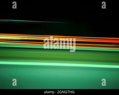 Les voies lumineuses vertes, orange et rouges des voitures roulant à grande vitesse sur l'autoroute la nuit, longue exposition Banque D'Images
