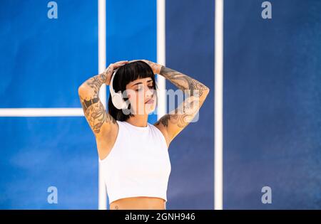Gros plan d'une fille espagnole avec des tatouages écoutant de la musique avec des écouteurs blancs Banque D'Images