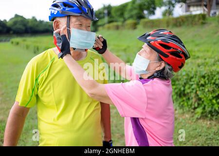 Un couple asiatique senior portant un masque médical et portant un vélo dans le parc Banque D'Images
