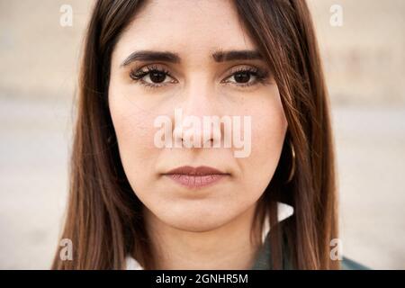 Gros plan d'une jeune femme aux yeux sombres regardant la caméra avec une expression sérieuse sur son visage. Banque D'Images