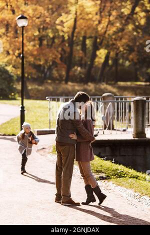 Famille amour et soins: Les parents couple baiser marchant dans le parc d'automne avec la jolie fille fille fille Banque D'Images