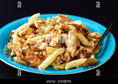 penne de pâtes alfredo de poulet à l'oignon caramélisé arrosé de pignons de pin et de parmesan râpé sur une assiette bleue sur fond noir, horizontale Banque D'Images