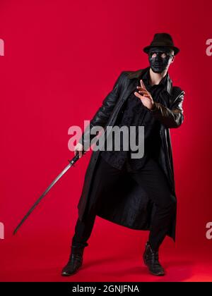 Un mystérieux assassin ninja dans un style noir. Un homme en cuir noir avec un manteau et un chapeau, couvre son visage avec un masque et utilise un katana. Photo Banque D'Images