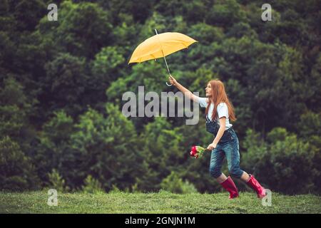 Joyeux gingembre, jeune fille en bottes rouges jouant avec son parapluie jaune. Danse sous la pluie Banque D'Images