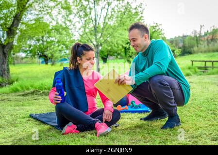 couple d'entraîneur personnel et une jeune étudiante femme enceinte discutant de l'horaire d'entraînement ensemble souriant en plein air. forme physique et mode de vie sain Banque D'Images