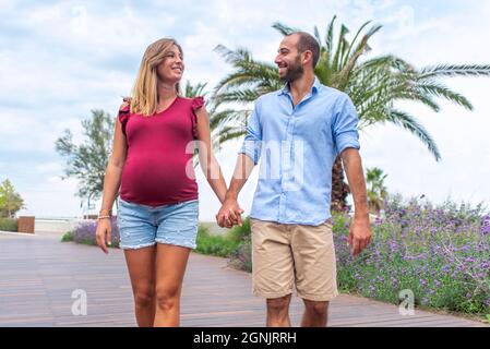 jeune couple heureux amoureux d'une femme enceinte et de son petit ami marchant dans la rue pour s'amuser en vacances. temps de famille de qualité tenant les mains Banque D'Images