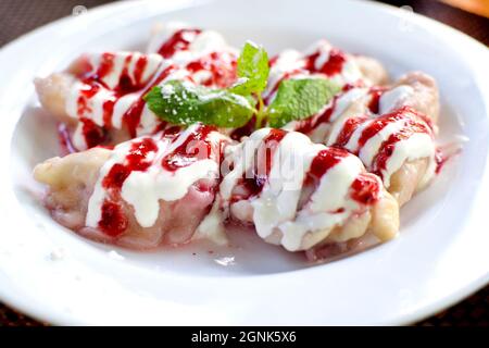 Boulettes de cerise arrosées de sirop de fraise sur une assiette blanche. Boulettes avec baies pour le petit déjeuner. Un plat sucré populaire en Europe de l'est Banque D'Images