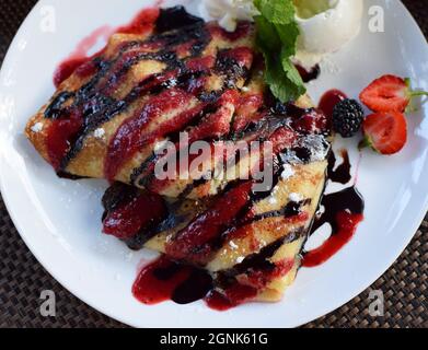 Crêpes farcies aux fruits et enrobées de chocolat et de sirops de baies. Servi avec des boules de crème glacée et des fraises. Crêpes fines, blini. Vue de dessus Banque D'Images