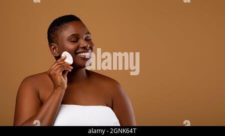 Portrait d'une femme noire curvy qui nettoie la peau avec un tampon en coton Banque D'Images