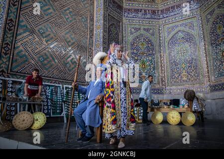 26 septembre 2021, Ouzbékistan, Samarkand : les Ouzbeks portent des robes traditionnelles pour une photo souvenir au monument historique du Reguistan à Samarkand. Le Registan était une place publique et un centre de l'ancien Samarkand pendant l'Empire Timurid, utilisé pour des proclamations royales, annoncées par des explosions sur d'énormes tuyaux de cuivre et des exécutions publiques. Photo: Oliver Weiken/dpa Banque D'Images