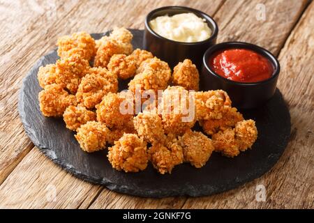 Pop-corn au poulet épicé pané frit profond servi avec deux sauces gros plan sur un tableau d'ardoise sur la table. Horizontal Banque D'Images