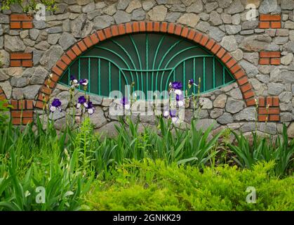 Un lit de fleurs avec des iris près d'une clôture pavée en pierre avec un treillis décoratif. Jardin art concept, lanshat design. Banque D'Images