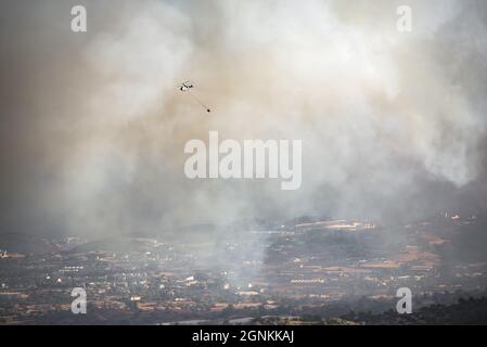 Hélicoptère avec seau d'eau volant dans de fortes fumées au-dessus de la zone rurale, luttant contre le feu de forêt Banque D'Images