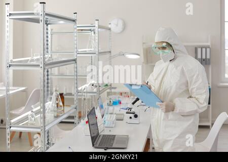 Un scientifique ou un médecin en costume médical de protection prend des notes sur l'expérience en laboratoire. Banque D'Images