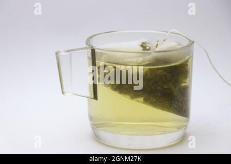 Sachet de thé vert dissolvant sa saveur de feuilles de plantes dans une tasse en verre avec de l'eau chaude Banque D'Images