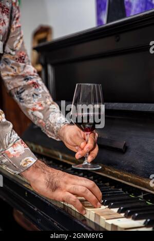 Vieux piano-clés classique et verre à vin. Un verre de vin rouge bordeaux dans un élégant verre à vin gravé reposant sur un clavier de piano. Banque D'Images