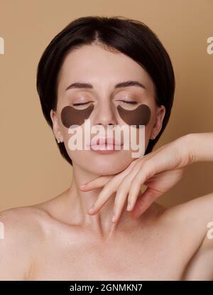 Jeune femme avec une peau saine et fraîche et propre pose sur fond beige , réduit sous la puffiness des yeux, des cercles sombres, applique des taches hydratantes sous l'ey Banque D'Images