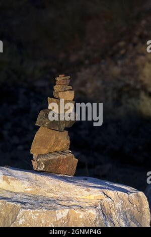 Empilez soigneusement des pierres sur une grande roche dans un format de mise au point et vertical sélectionné avec un espace de copie dans une zone plus sombre derrière une petite tour de roche Banque D'Images