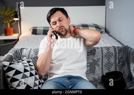 Handicapé homme douloureux avec un corset de cou parlant au téléphone à la maison. Homme avec un traumatisme de colonne vertébrale dans le cou étrésillon cervical appeler compagnie d'assurance pour l'aide médicale Banque D'Images