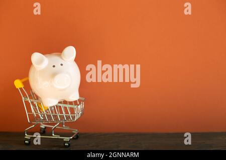 Une banque de porc rose dans un panier sur un bureau en bois. Fond de mur rouge Banque D'Images