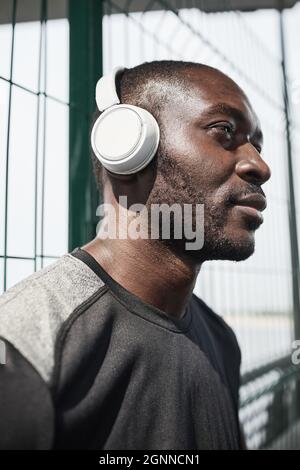 Gros plan sur un jeune africain dans un casque sans fil, en regardant loin avec une vue pensive en plein air Banque D'Images