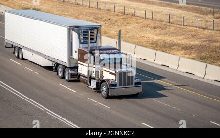 Semi-remorque American idol Big rig à capot classique brun industriel avec tuyaux d'échappement chromés transportant des marchandises commerciales congelées dans une semi-remorque reefer Banque D'Images